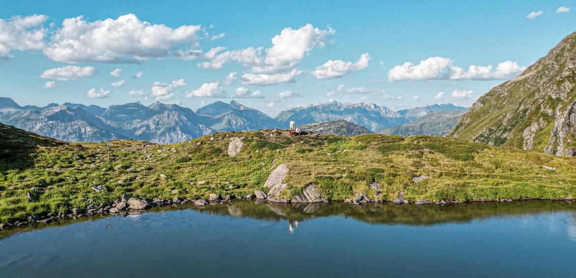 Ein Bergsee im Sommer mit zwei Personen in Hintergrund. | © Silvretta Montafon - Vanessa Strauch