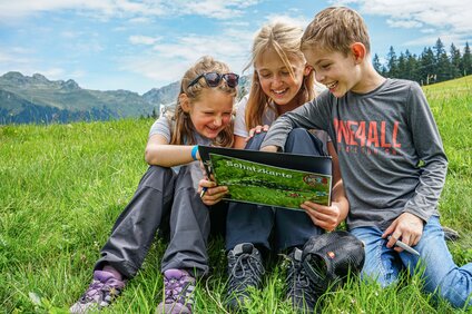 Schatzsuche - Silvretta Montafon | © Silvretta Montafon - Vanessa Strauch Drei Kinder sitzen auf einer Wiese und lesen eine Schatzkarte in der Silvretta Montafon. | © Silvretta Montafon - Vanessa Strauch