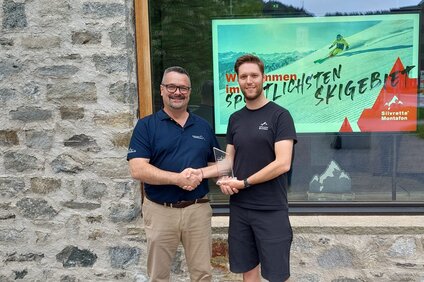 Auszeichnung 2. Platz umweltschonendes Skigebiet - Silvretta Montafon | © Silvretta Montafon Zwei Männer überreichen sich einen Award zum umweltschonenden Skigebiet vor der Alpin Sport Zentrale in Schruns | © Silvretta Montafon