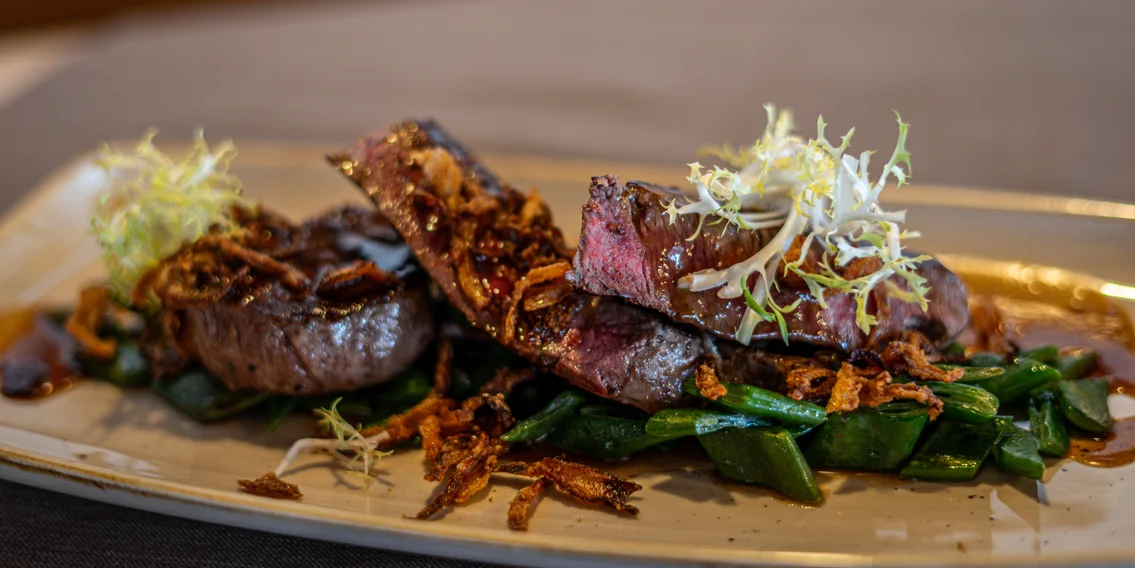 Ein zart gebratenerer Zwiebelrostbraten mit Speckbohnen im Kapellrestaurant | © Silvretta Montafon - Vanessa Strauch