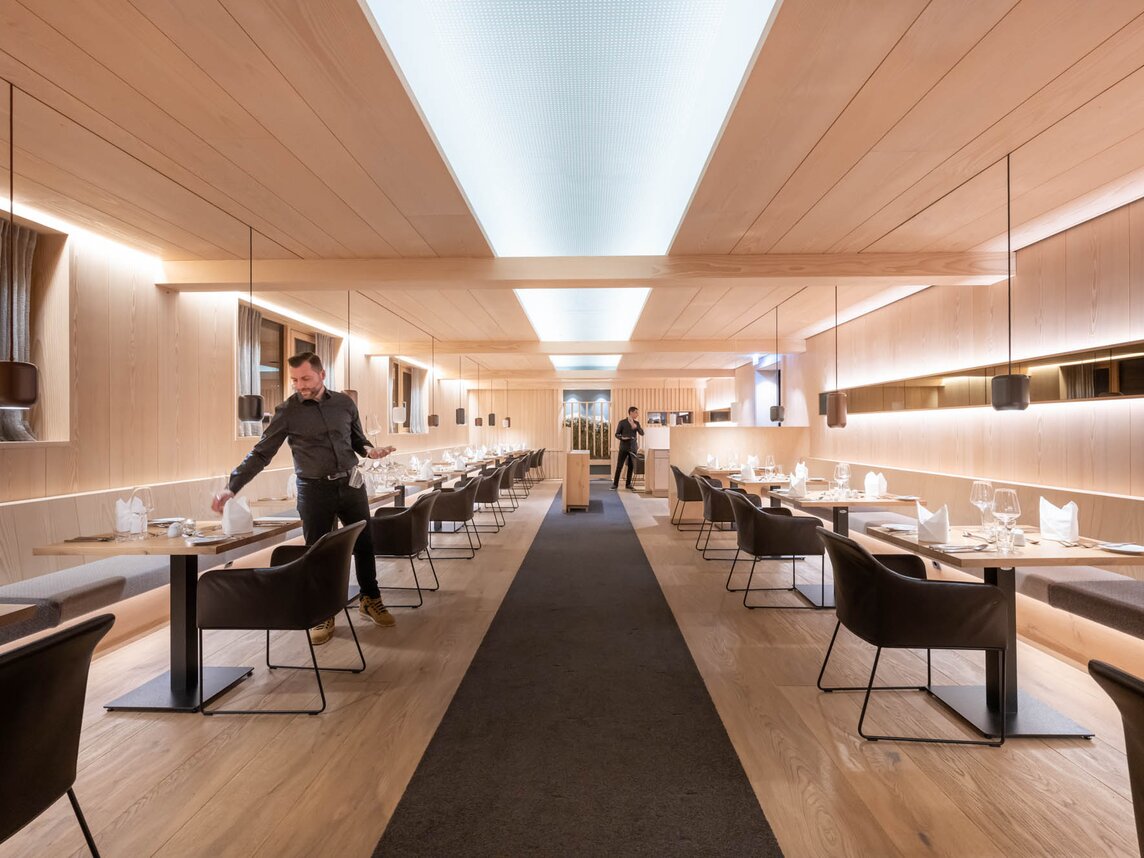 Simons Alpenbrasserie im Sporthotel Silvretta Montafon in Gaschurn | © Silvretta Montafon - blateral Zwei Kellner decken die Tische im Restaurant mit gemütlichen anthrazitfarbenen Sesseln und Holzambiente | © Silvretta Montafon - blateral