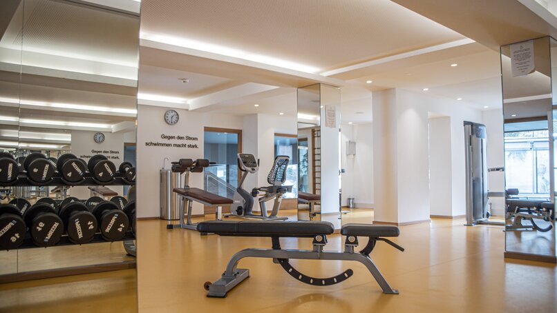Fitness im Sporthotel Silvretta Montafon | © Silvretta Montafon - Mara Baues Ein Fitnessraum mit Trainingsgeräten und Hanteln mit gelbem Boden und Spiegeln | © Silvretta Montafon - Mara Baues